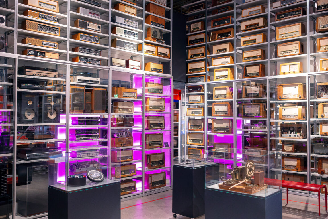 Vanhoja radioita hyllyillä ja esineitä vitriineissä.