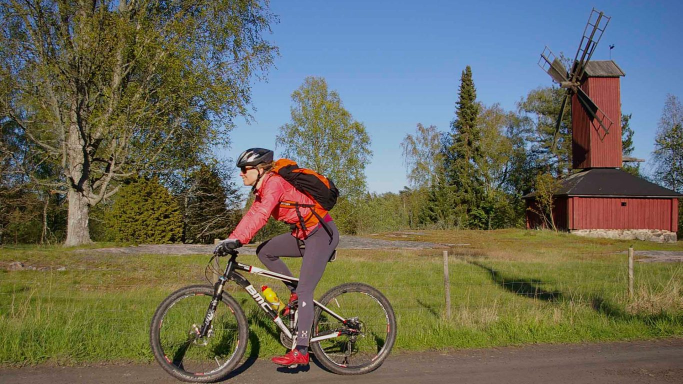 Nainen pyöräilemässä maalaismaisemissa, taustalla tuulimylly